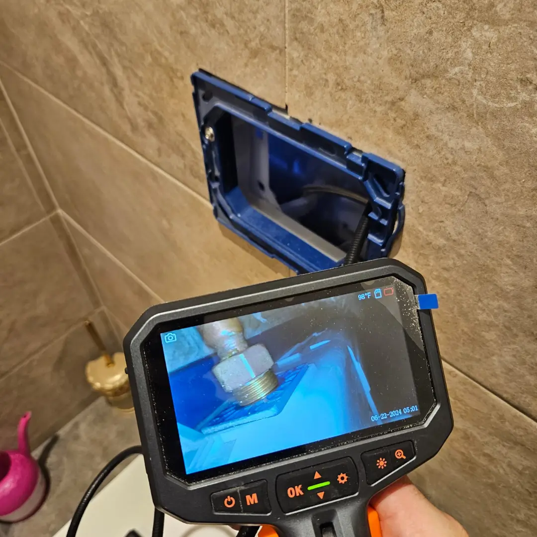 Endoscope camera inspecting hidden pipework behind a tiled wall, aiding non-destructive leak detection.